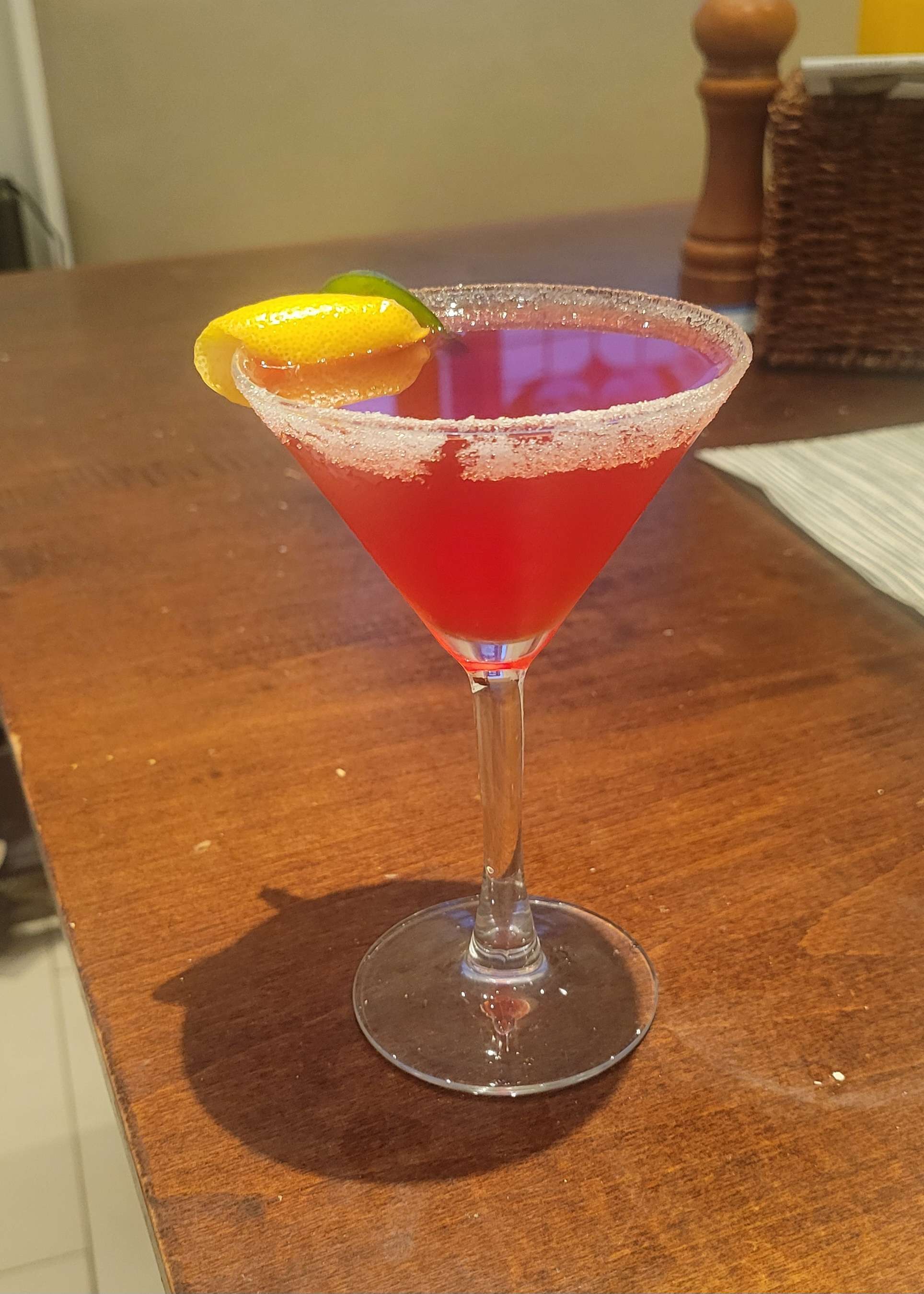 Image of the Fukase's Cherry-Peño Lemon Drop cocktail, a bright pinkish-red drink in a martini glass with a white sugar rim, garnished with a jalapeño slice and a lemon twist.